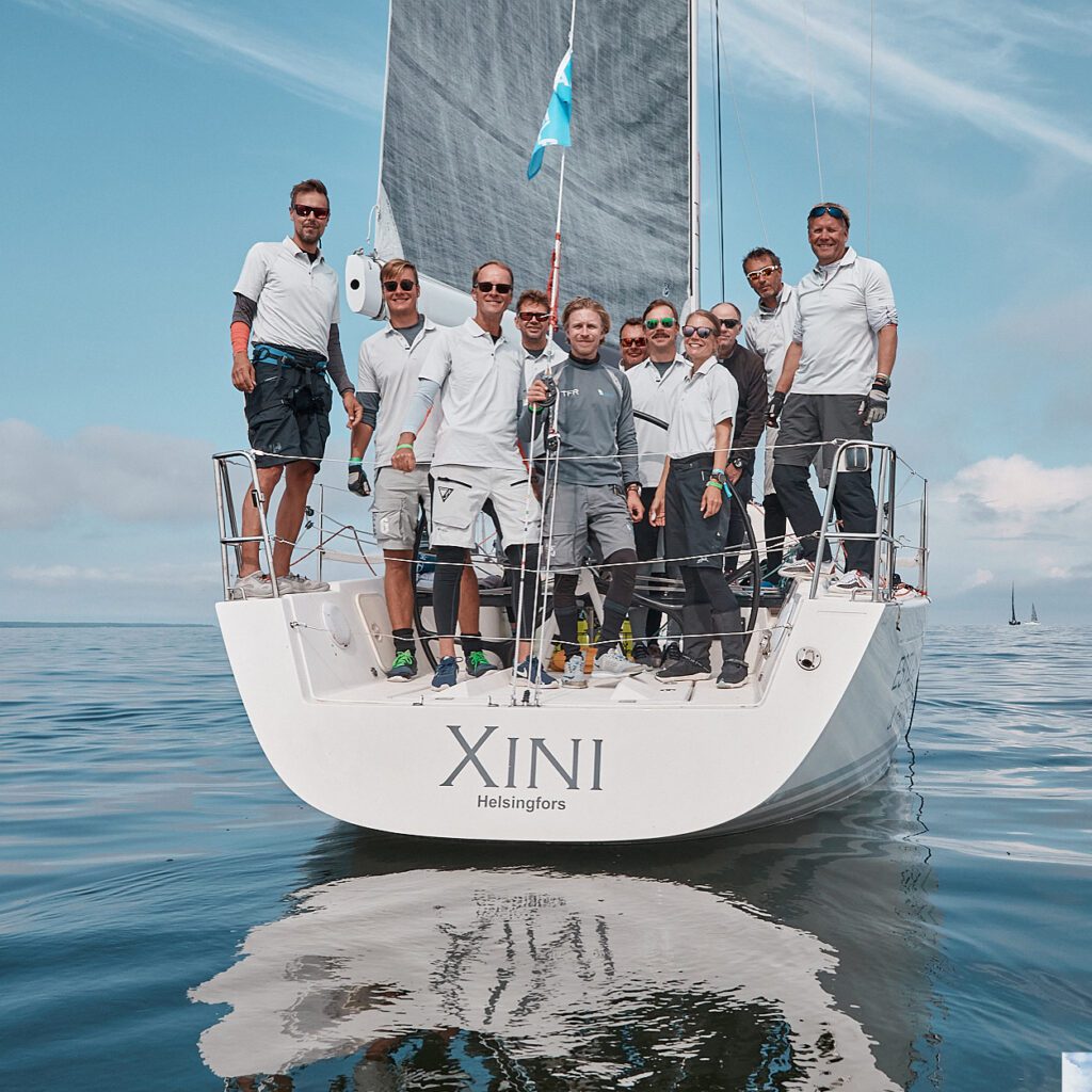 The crew of "Xini" poses at the stern on a calm day, with the sea like glass. 