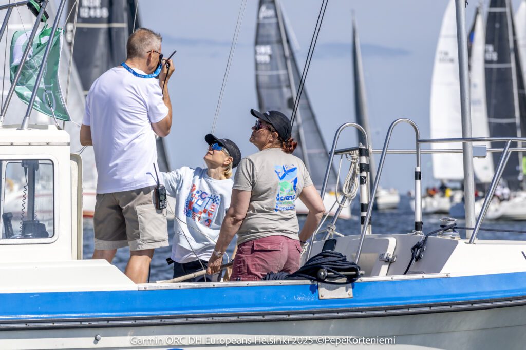 Noora on the race committee boat in her ORC 2025 sweatshirt on a sunny day, looking up to another committee member talking on a handheld radio. 