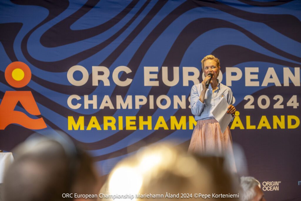 Noora speaks onstage at the ORC European Championship, the event banner behind her. 
